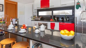 Una cocina moderna con encimera negra, electrodomésticos de acero inoxidable y detalles en rojo.