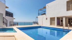 Una piscina con un cielo azul despejado al fondo, rodeada por un edificio blanco con balcones.