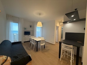 Ein modernes Wohnzimmer mit Sofa, Esstisch und Stühlen, einem Fernseher und einem Balkon mit Blick.