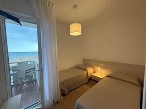 Een hotelkamer met twee bedden, een balkon met een tafel en stoelen, en uitzicht op het strand.