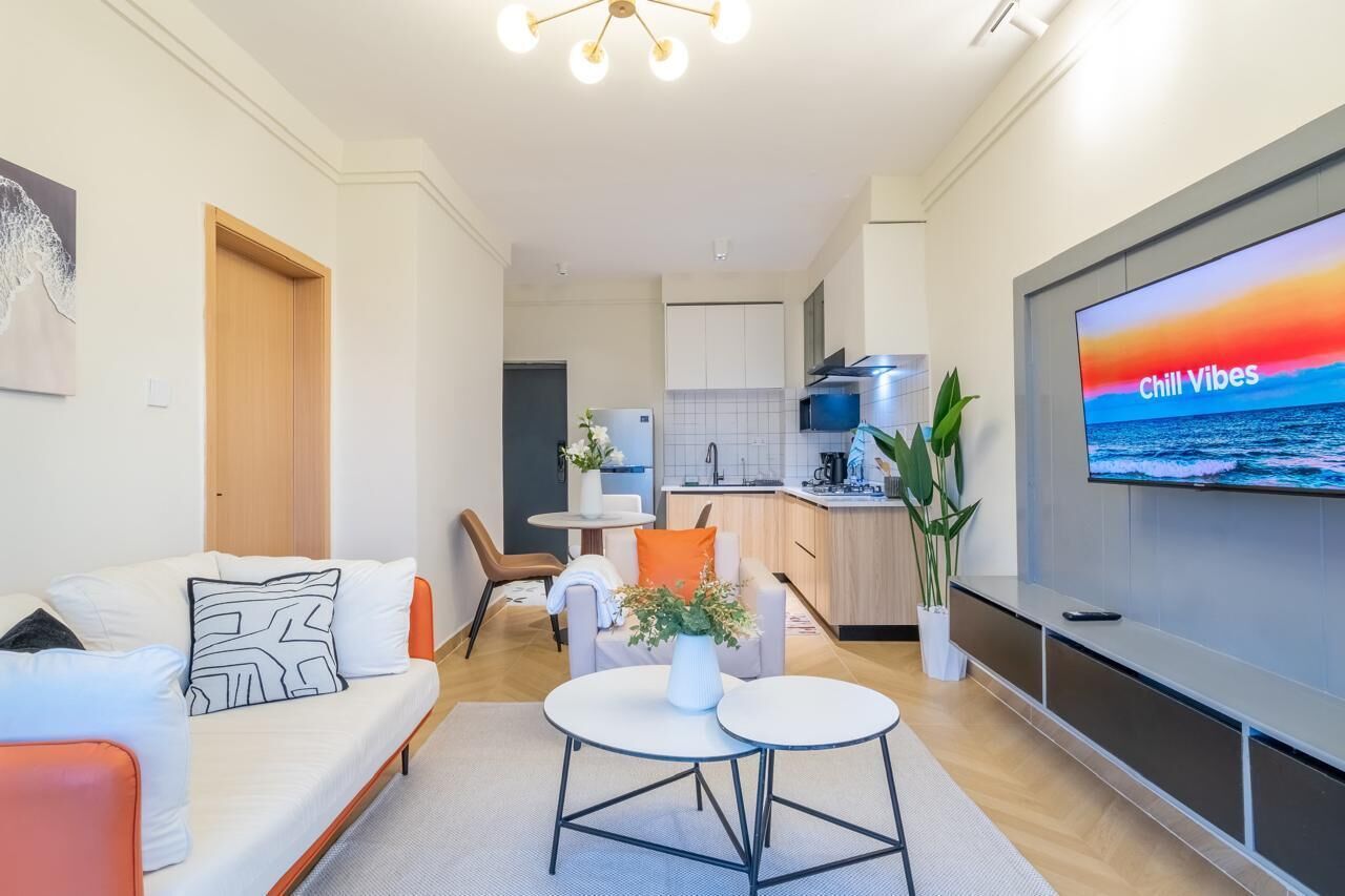 A modern living room with a sofa, two tables, a TV displaying 'Chill Vibes,' and a kitchen in the background.