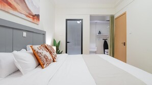 Habitación de hotel con cama, cabecero gris, puerta y armario con cortina verde.
