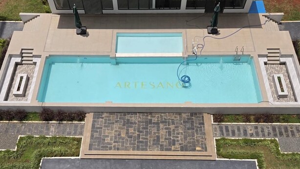 Una piscina con el texto 'ARTESANO', rodeada por un camino de piedra y follaje.