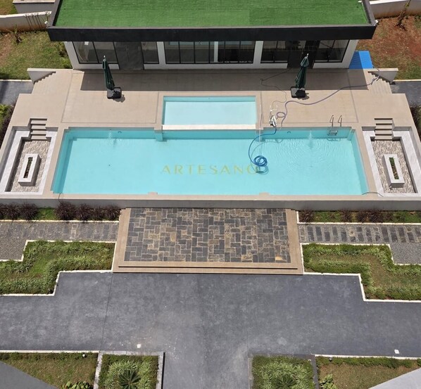 Ein Swimmingpool mit der Aufschrift 'ARTESANO', umgeben von einem Steinpfad und Grünflächen.