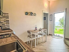 A kitchen with a gas stove, a dining table with chairs, a small refrigerator, and a view of the outdoors through a glass door. - Pierina by Interhome (Finale Ligure)