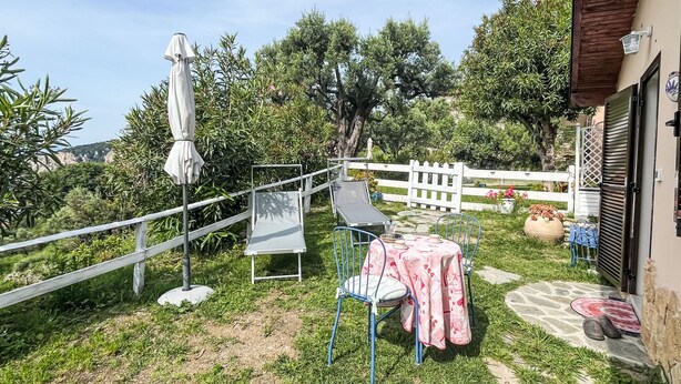 Um pátio com mesa e cadeiras, um guarda-sol branco e uma cerca branca.