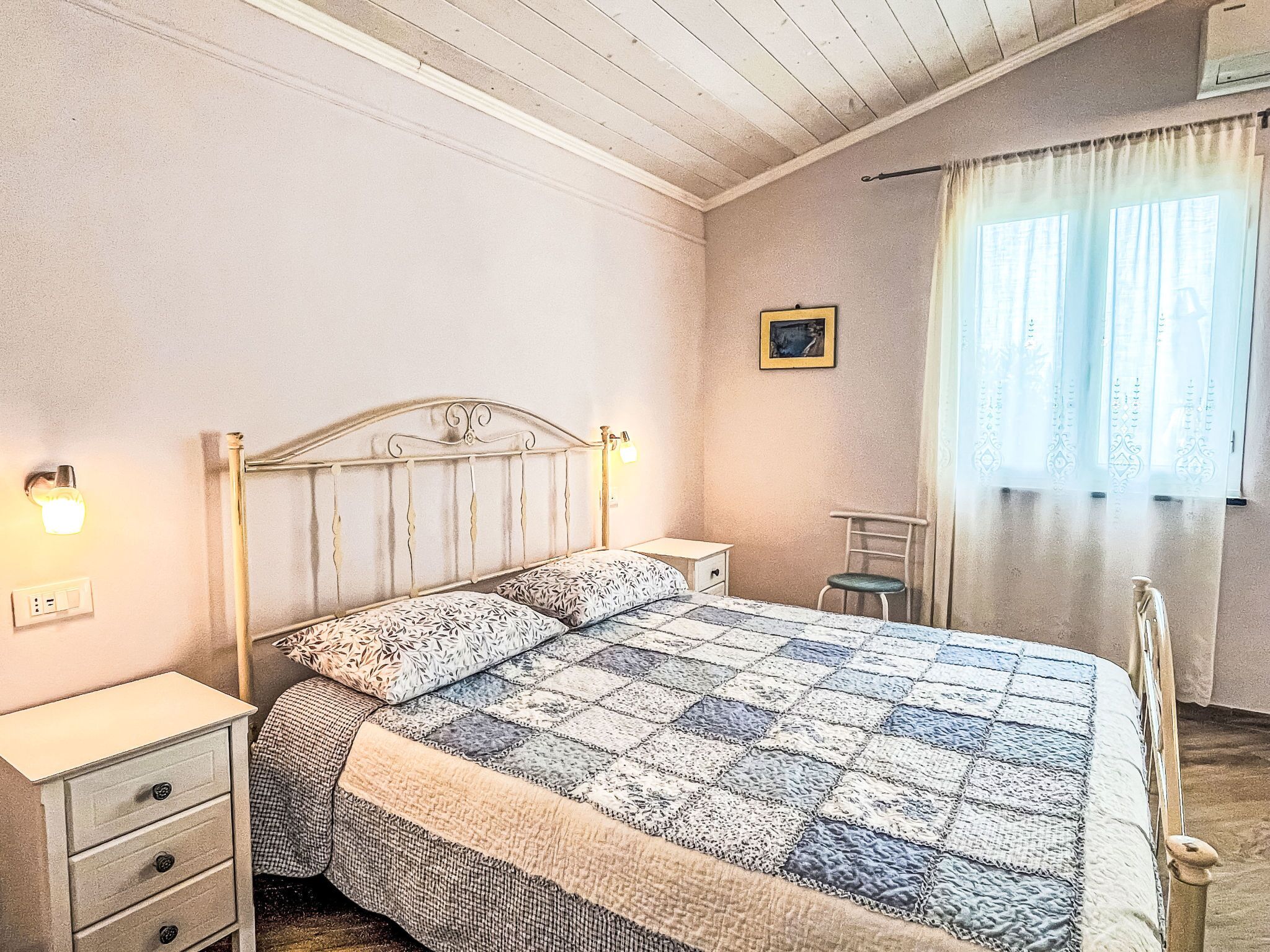 A bedroom with a bed, bedside tables, a chair, a picture on the wall, and a window with curtains.