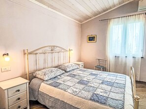 A bedroom with a bed, bedside tables, a chair, a picture on the wall, and a window with curtains. - Pierina by Interhome (Finale Ligure)