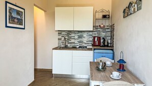 Uma cozinha compacta com armários brancos, painel de azulejos, uma cafeteira e uma pequena mesa com um bule e xícaras.