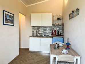 A compact kitchen with white cabinets, a tiled backsplash, a coffee maker, and a small table with a teapot and cups. - Pierina by Interhome (Finale Ligure)
