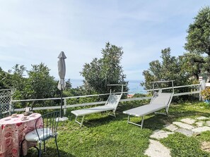 A patio with a table, chairs, and a bench, surrounded by greenery and overlooking a body of water. - Pierina by Interhome (Finale Ligure)