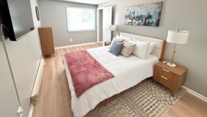 A bedroom with a bed, bedside table, lamp, and a painting on the wall. - Twin Oaks Extended Stay One Bedroom - 2817 Apt 13 (Syracuse)