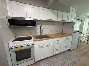 Una cocina moderna con armarios blancos, un microondas de acero inoxidable, horno empotrado y encimera de madera.