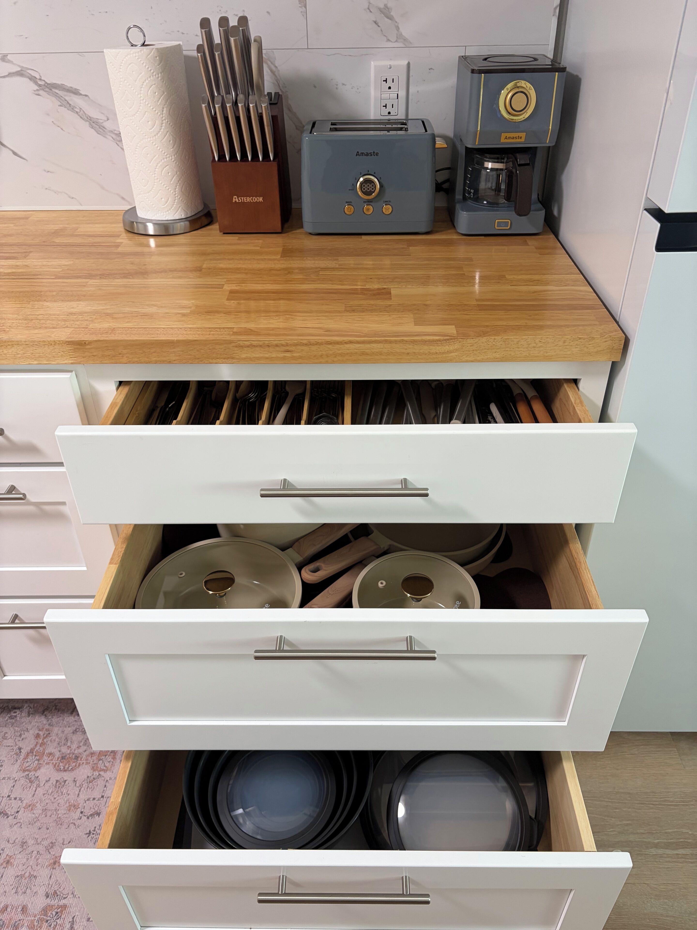 Una cocina con tostadora, cafetera y un cajón con utensilios de cocina.