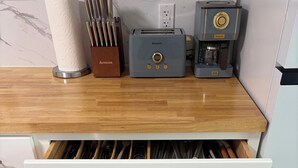 A kitchen with a toaster, coffee maker, and a drawer with kitchen utensils. - Twin Oaks Extended Stay One Bedroom - 2817 Apt 13 (Syracuse)