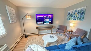 A modern living room with a flat-screen TV, a sofa, two armchairs, a coffee table, and a floor lamp. - Twin Oaks Extended Stay One Bedroom - 2817 Apt 13 (Syracuse)