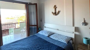 A bedroom with a bed, a ceiling fan, a balcony, and a wall-mounted anchor decoration. - Small villa in quiet setting a few minutes from the sea (Villasimius)