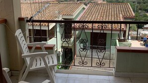 A balcony with a view of a town, a tiled floor, and a metal railing. - Small villa in quiet setting a few minutes from the sea (Villasimius)