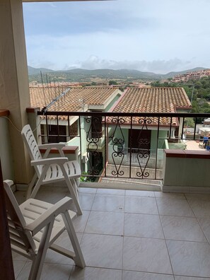 A balcony with a view of a town, a tiled floor, and a metal railing. - Small villa in quiet setting a few minutes from the sea (Villasimius)