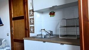 A compact kitchen with a wooden door, white cabinets, a stainless steel sink, and a small fruit decoration. - Small villa in quiet setting a few minutes from the sea (Villasimius)