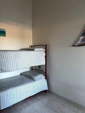 A bunk bed with striped bedding in a room with a tiled floor and a plain wall. - Small villa in quiet setting a few minutes from the sea (Villasimius)