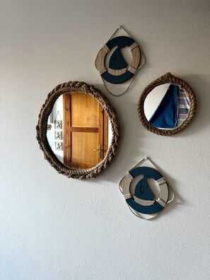 Quatre miroirs encadrés de corde, fixés au mur, un grand miroir avec un reflet de porte en bois, et un plus petit miroir à motifs à carreaux.