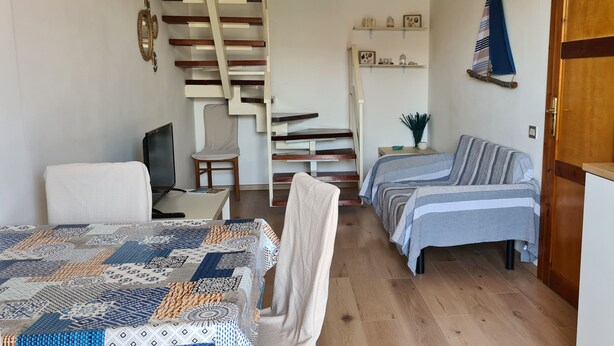 A compact room with a bed, a chair, a desk, a small table, a staircase, and a kitchen area. - Small villa in quiet setting a few minutes from the sea (Villasimius)
