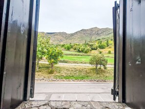 Blick durch offene Türen eines Gebäudes auf eine Straße und grüne Felder im Hintergrund.
