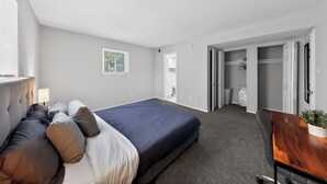 Quarto de hotel moderno com cama, mesa de cabeceira, abajur e vista para o corredor.
