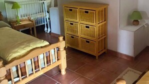 Ein Schlafzimmer mit einem hölzernen Bett, einem Babybett, Korbwäsche und einer Wandleuchte.