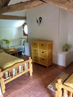 Ein Schlafzimmer mit einem hölzernen Bett, einem Babybett, Korbwäsche und einer Wandleuchte.