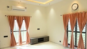 Una habitación con dos ventanas, un reloj de pared, un equipo de aire acondicionado y un mueble pequeño.