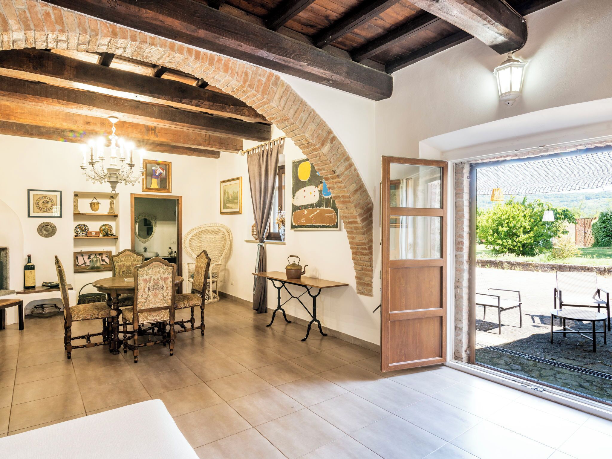 A dining area with a wooden table, chairs, and a chandelier. There is a door leading to an outdoor patio.