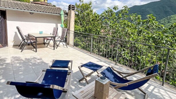 Een terras met een tafel en stoelen, een bijzettafeltje met een speaker, en uitzicht op een berg.
