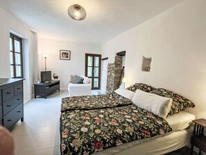 A bedroom with a bed, dresser, television, and a stone wall. - Laetitia by Interhome (Pieve di Teco)