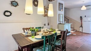 Een eetruimte met een houten tafel, stoelen, hangende吊り下げランプ, en een keuken op de achtergrond.