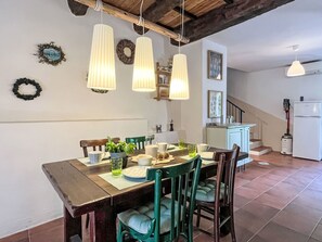 A dining area with a wooden table, chairs, hanging pendant lights, and a kitchen in the background. - Laetitia by Interhome (Pieve di Teco)
