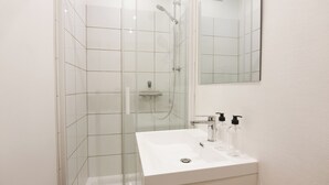 Un bagno moderno con cabina doccia in vetro, lavabo bianco e specchio sopra.