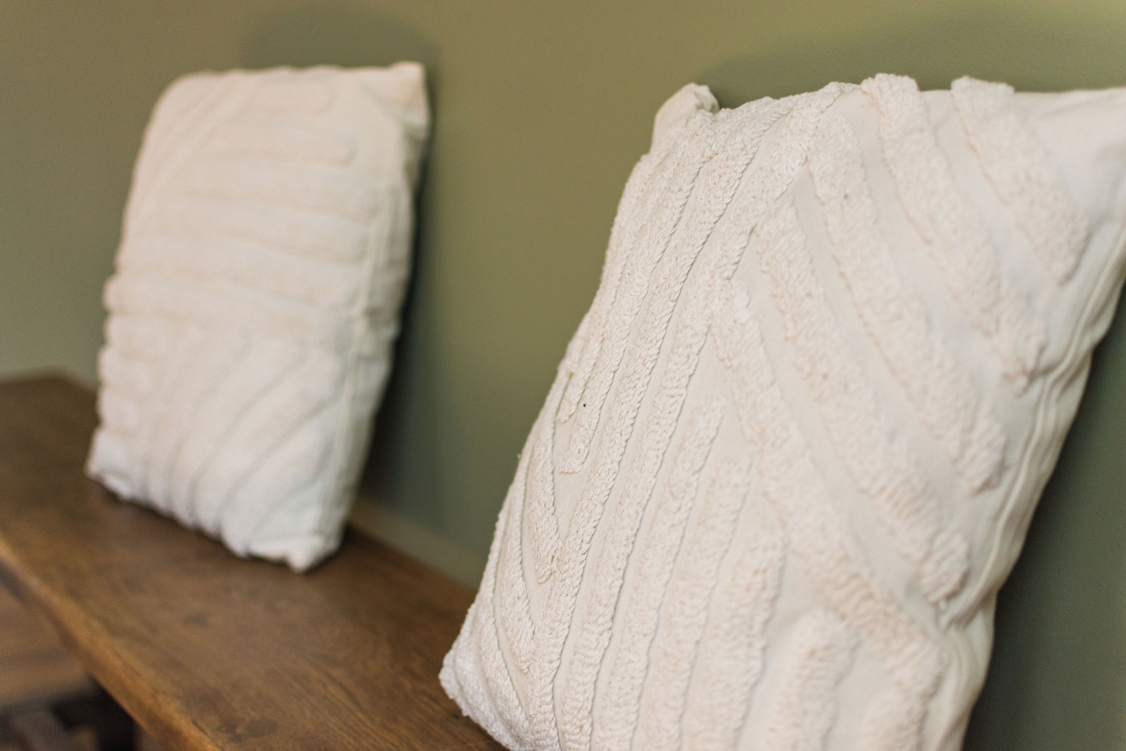 Two white pillows on a wooden bench against a green wall.
