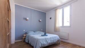Una camera da letto con un letto, un comodino, una finestra con tende, un termosifone e un punto luce a parete.