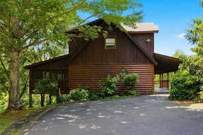 A rustic log cabin with a covered porch, surrounded by lush greenery. - Hibernation Station: Cozy Creekside Cabin (Sevierville)