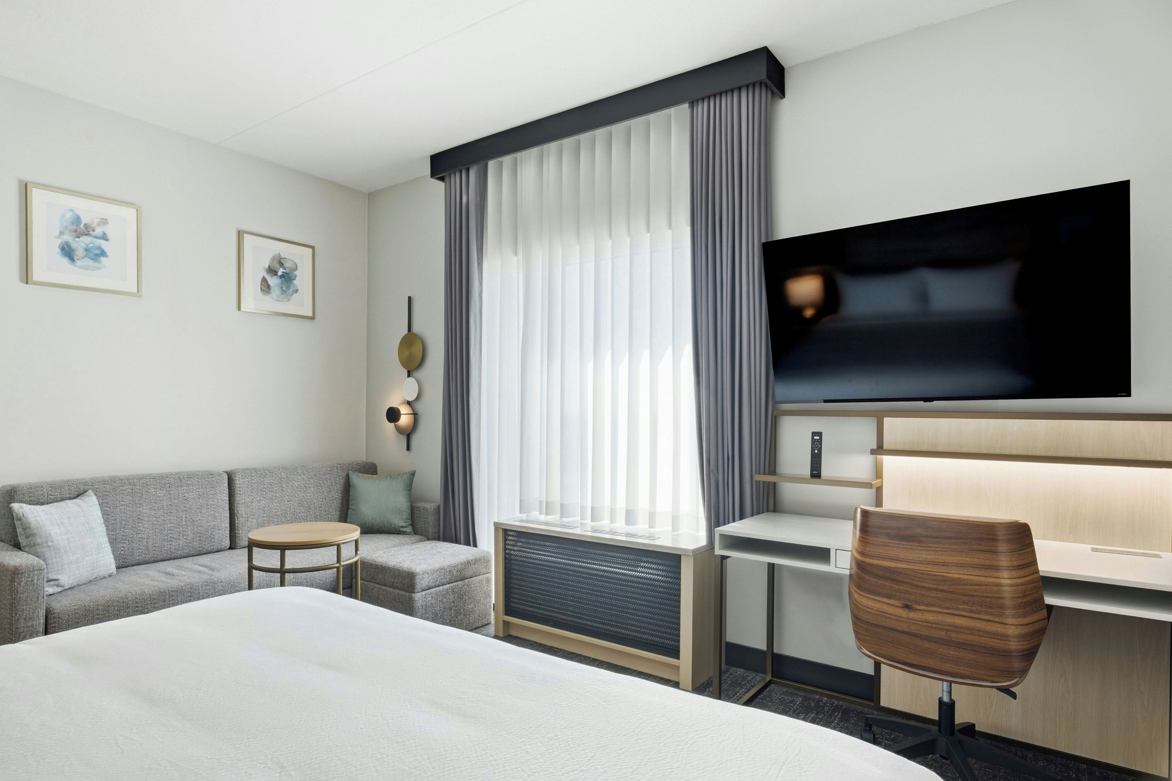 A hotel room with a large bed, a desk with a chair, a television, and a window with curtains.