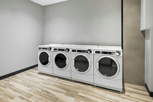 Un cuarto de lavandería con cuatro lavadoras de carga frontal, suelo de madera y paredes lisas.