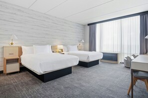 Habitación de hotel con dos camas, un escritorio y un amplio ventanal con cortinas.