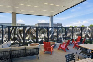 An outdoor seating area with a modern design, featuring a mix of red and grey furniture, a decorative fence with circular cutouts, and a clear view of the sky. - TownePlace Suites by Marriott Vaughan (Vaughan)