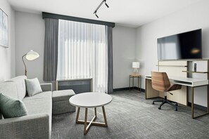 A modern hotel room with a grey sofa, a round table, a desk with a chair, a TV, and a window with curtains. - TownePlace Suites by Marriott Vaughan (Vaughan)