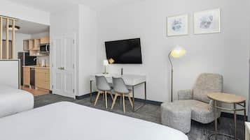Ein Hotelzimmer mit einem Bett, einem Schreibtisch mit zwei Stühlen, einem Fernseher, einer Lampe, einem kleinen Tisch und einem Schlafsofa.
