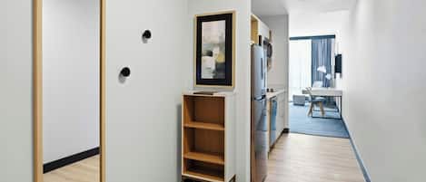 Een moderne hotelkamer met een houten vloer, een inbouwkleerkast, een keukenhoek met een koelkast en magnetron, en een eethoek met een tafel en stoelen.