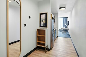 A modern hotel room with a wooden floor, a built-in wardrobe, a kitchen area with a refrigerator and microwave, and a dining area with a table and chairs. - TownePlace Suites by Marriott Vaughan (Vaughan)