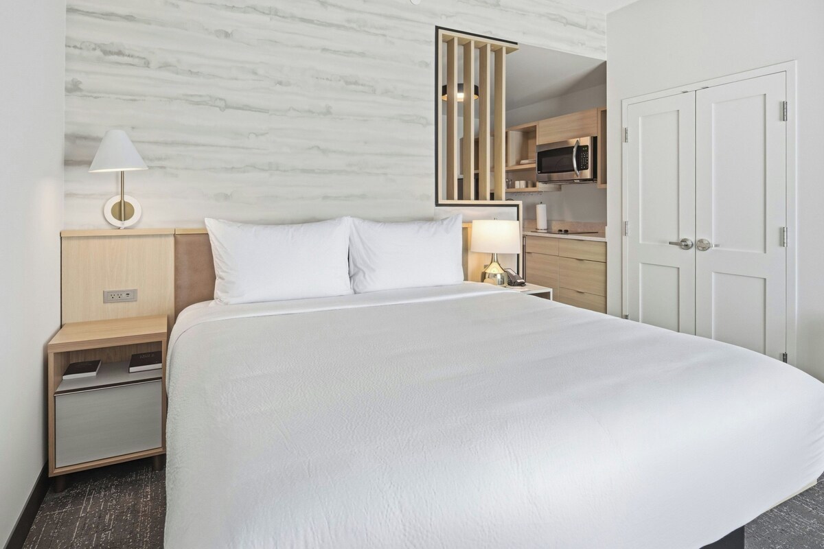 A hotel room with a bed, bedside tables, a lamp, a wardrobe, and a microwave.
